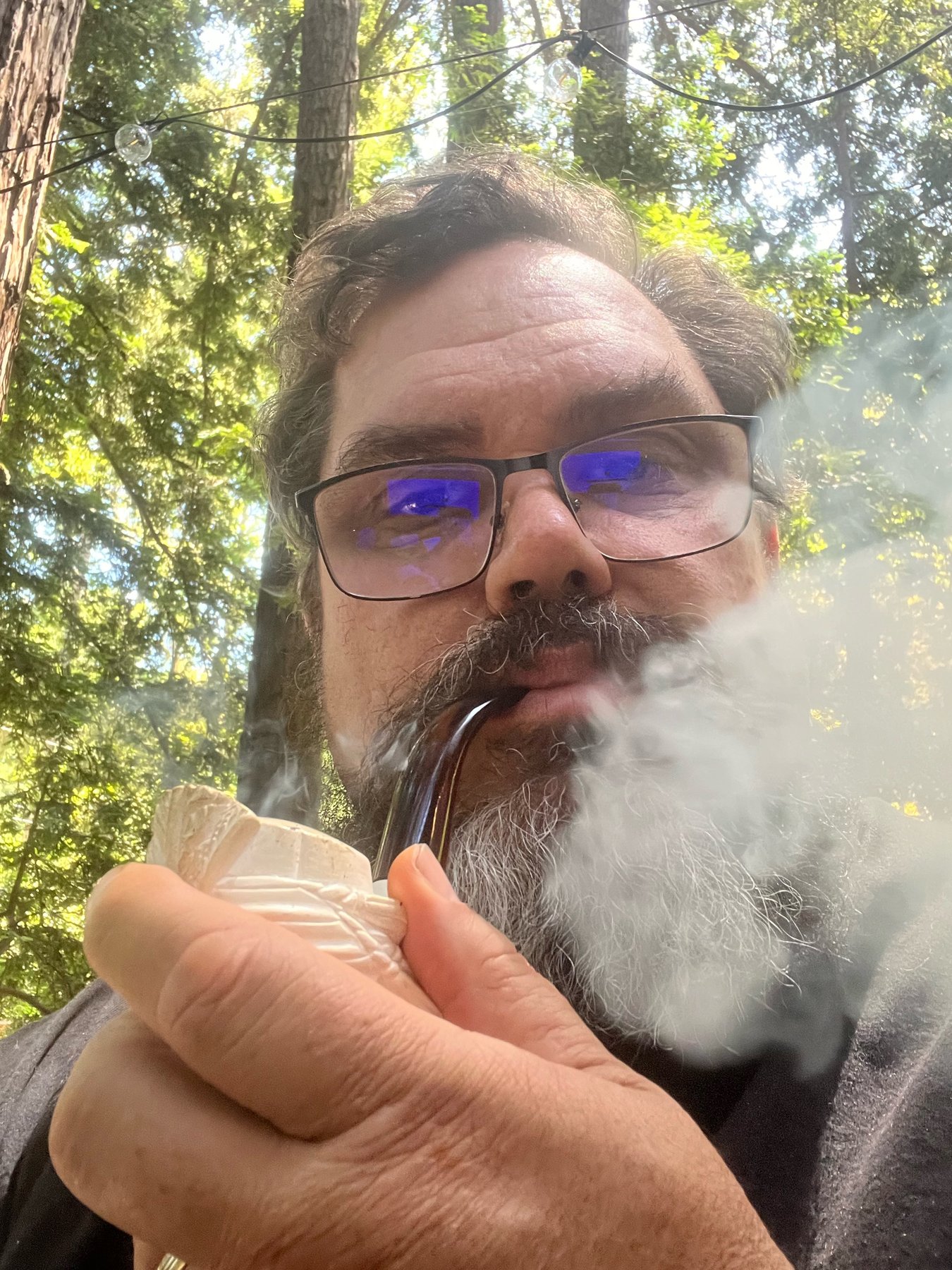 Nate Bunney outdoors among redwoods, with pipe smoke curling beside his face